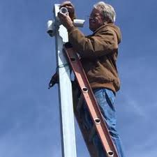 A man on a ladder painting the side of a pole.