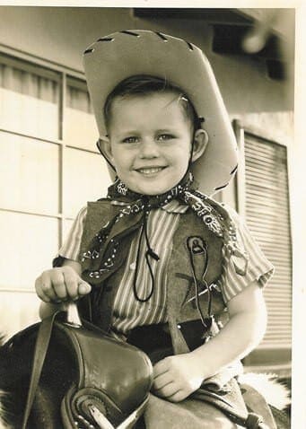 A young boy in cowboy attire holding a hat.